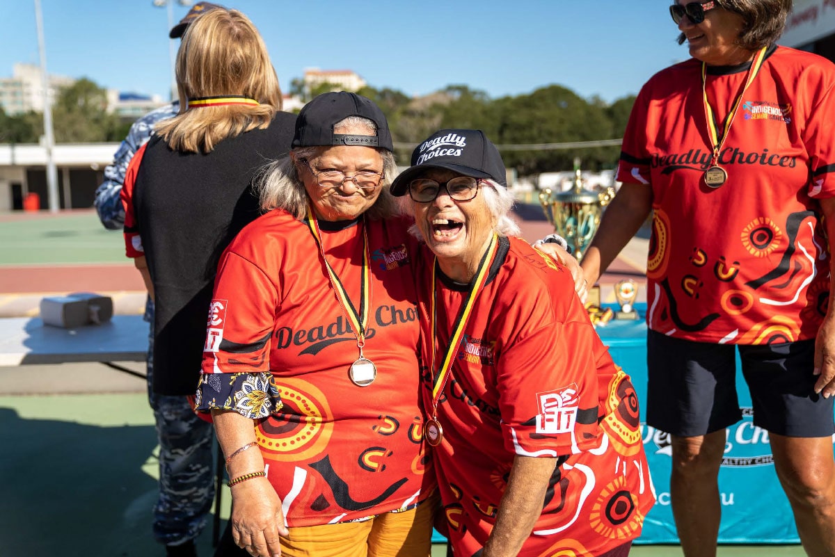 Elders wearing Deadly Choices shirts smiling with their arms around their shoulders.